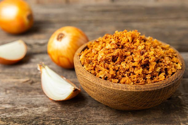 Crispy fried onions in a bowl on a wooden table. Roasted Onions. Seasoning for dishes. Spices. Salad dressing. Space for text. Copy space