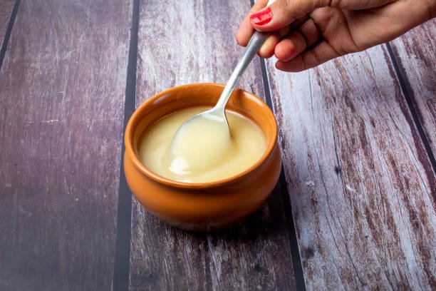 Pure cow ghee in ceramic bowl on wooden background with ghee spoon in hand